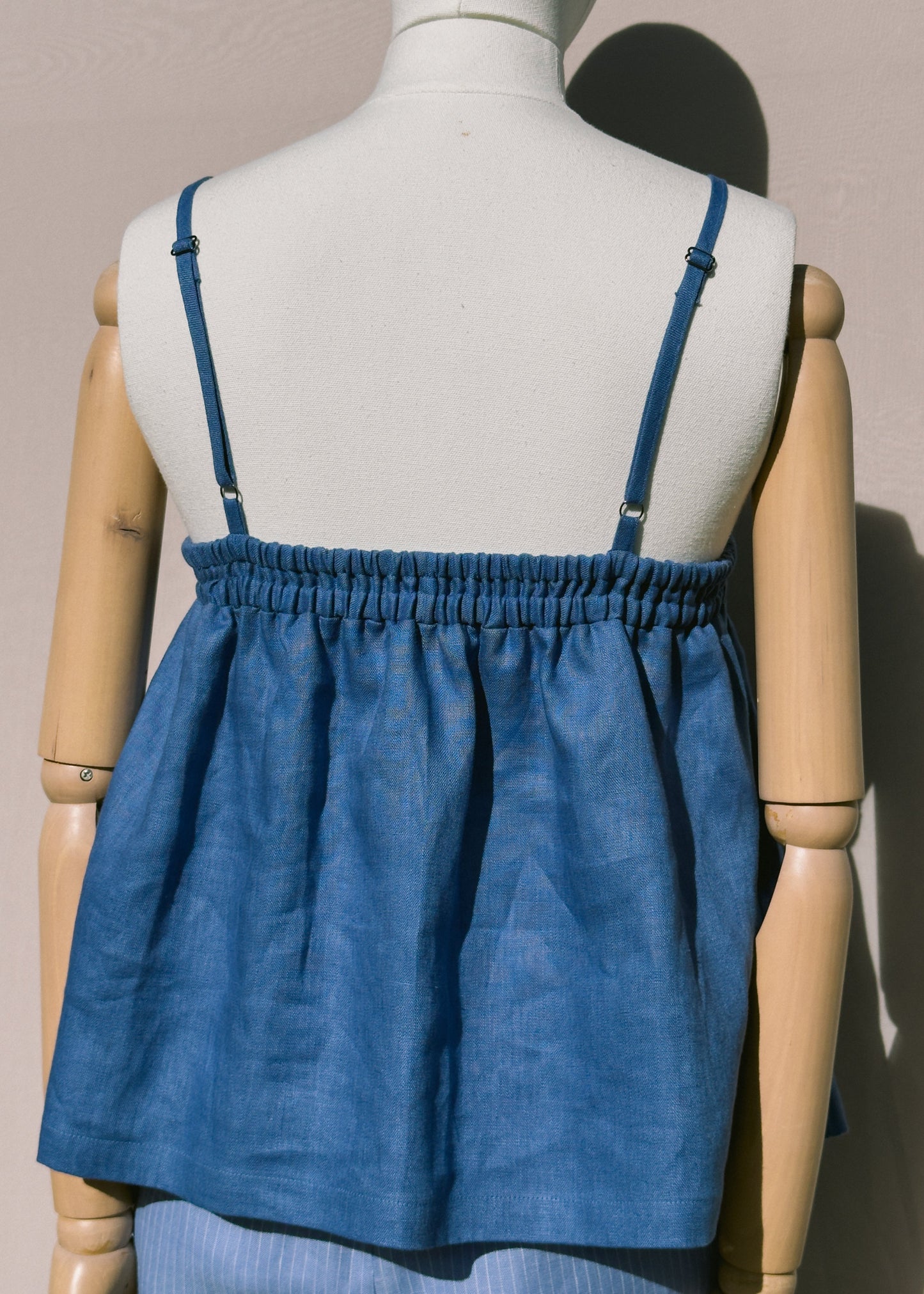 Blue linen top with gathers on a mannequin against a plain background showing back