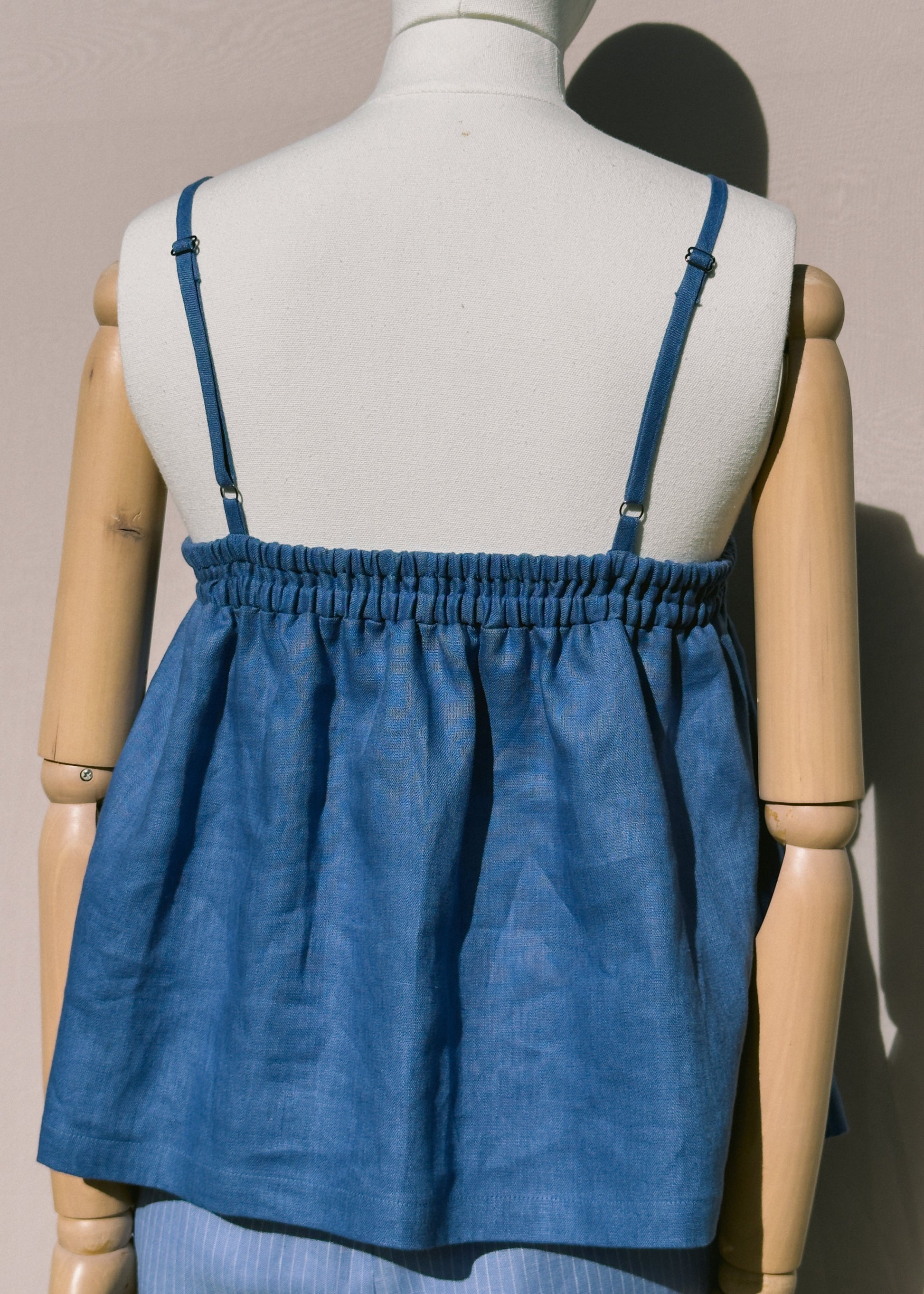Blue linen top with gathers on a mannequin against a plain background showing back