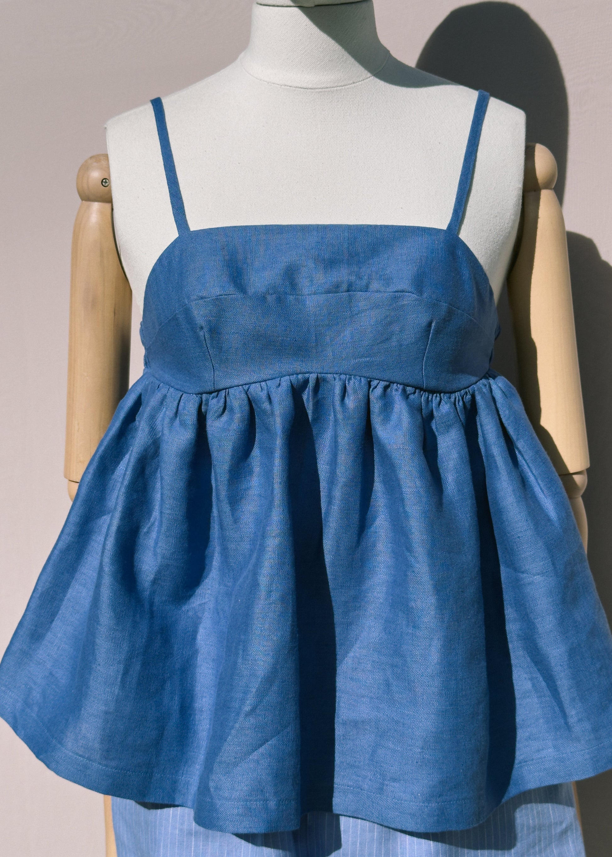 Blue linen top with gathers on a mannequin against a plain background