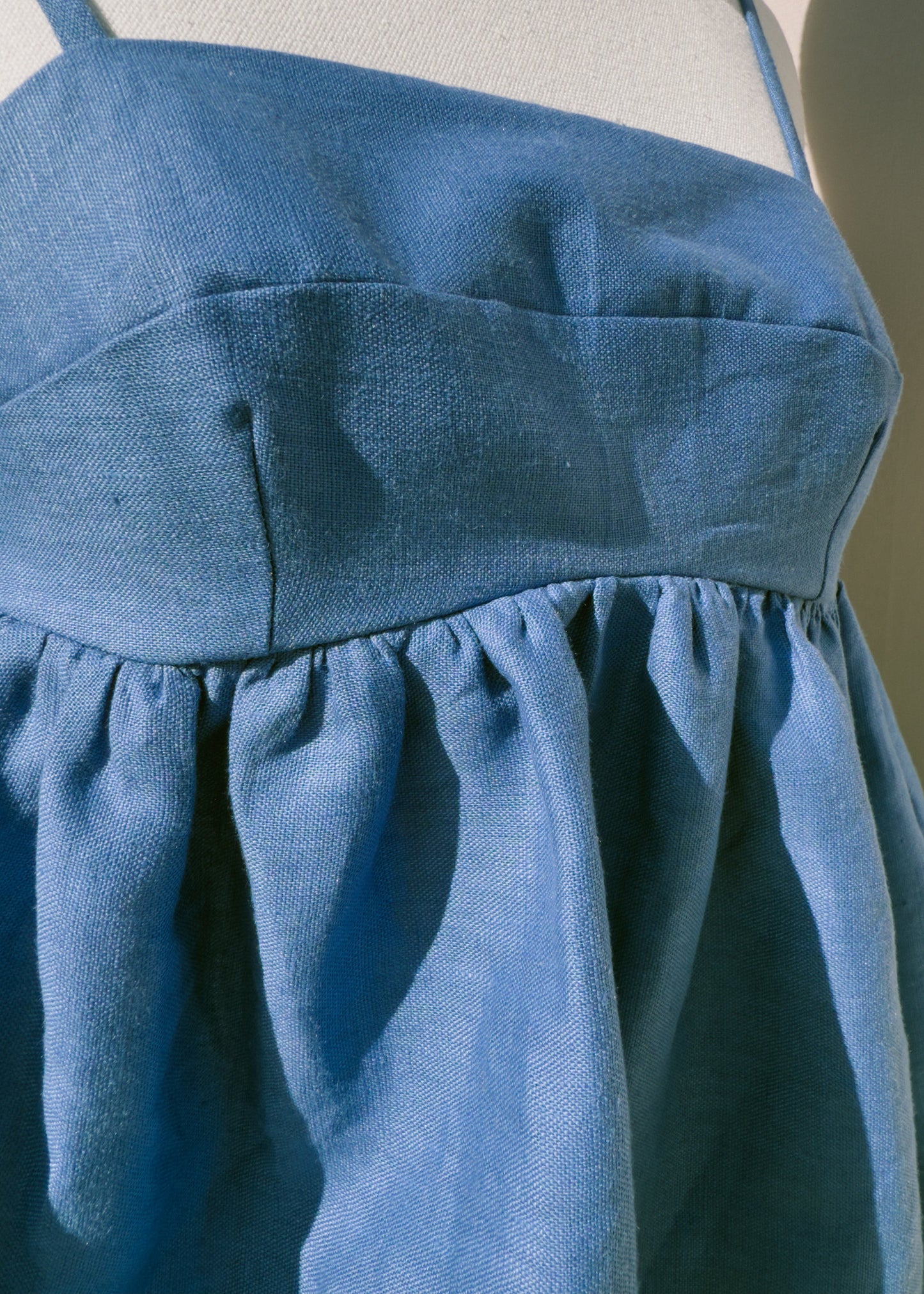 Close up of front of blue linen top with gathers on a mannequin against a plain background