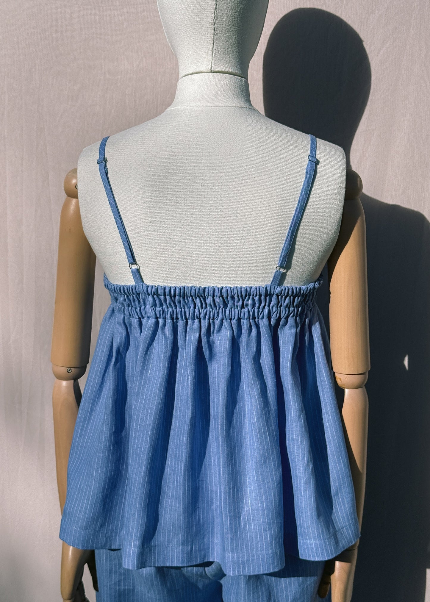 Blue striped linen top with elastic back on a mannequin in front of a plain beige background