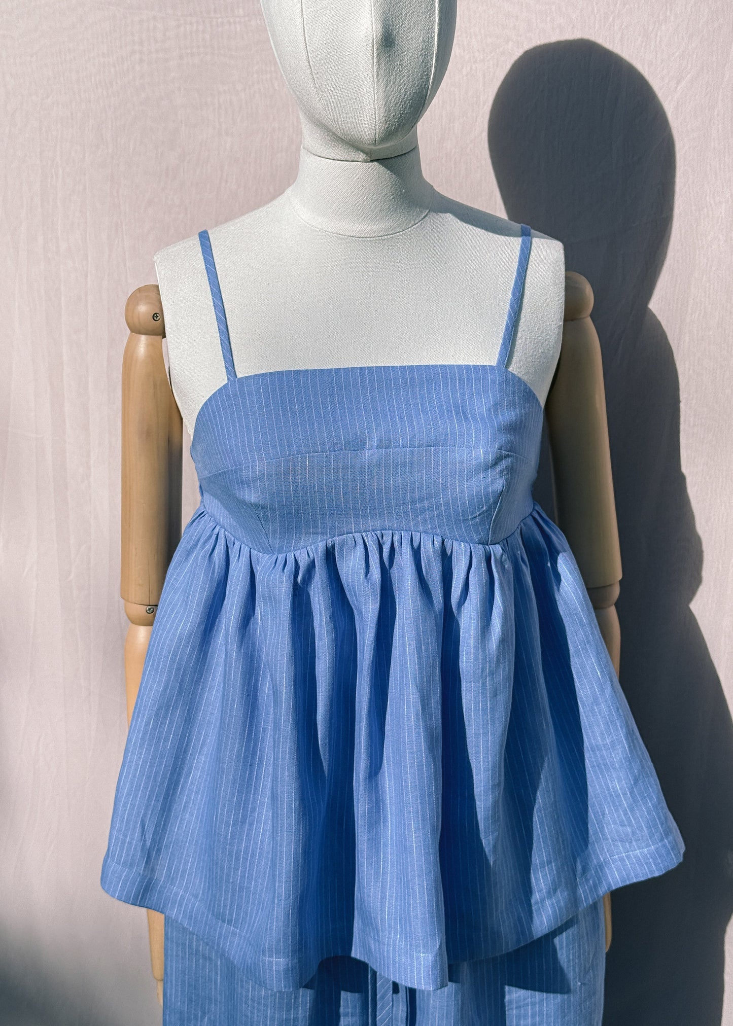 Blue striped linen top with gathers on a mannequin in front of a plain beige background
