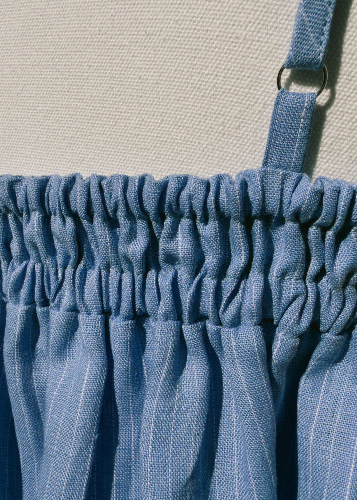 Close up back blue linen top with gathers on a mannequin in front of a plain beige background