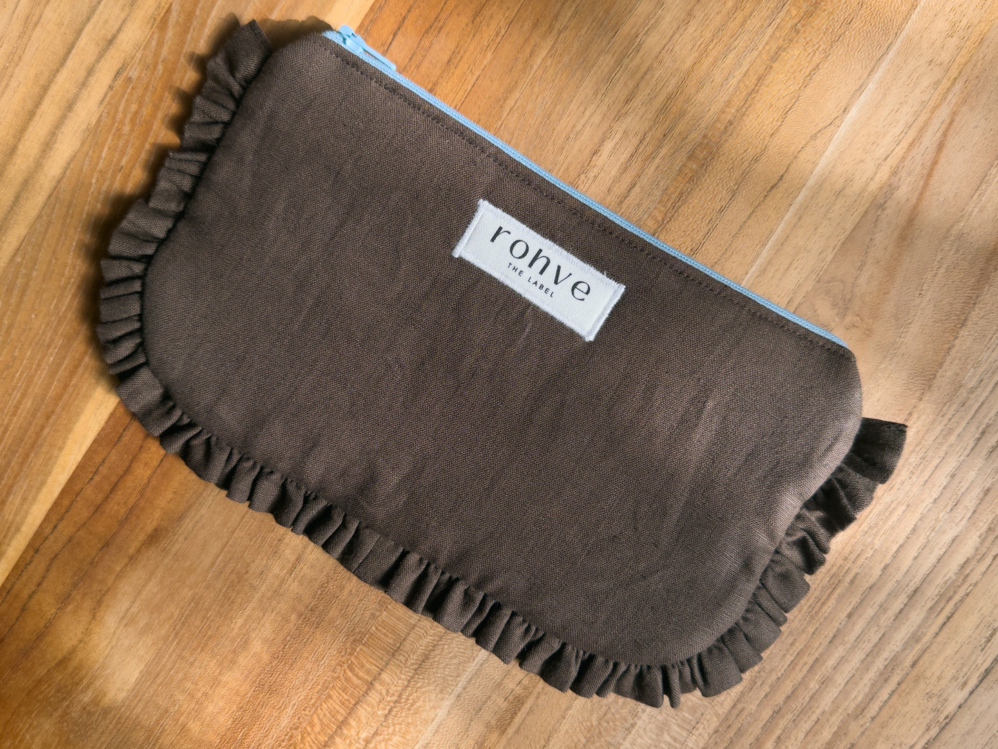 A brown fabric pouch with a ruffled edge and a white label reading 'rohve' on a wooden surface.