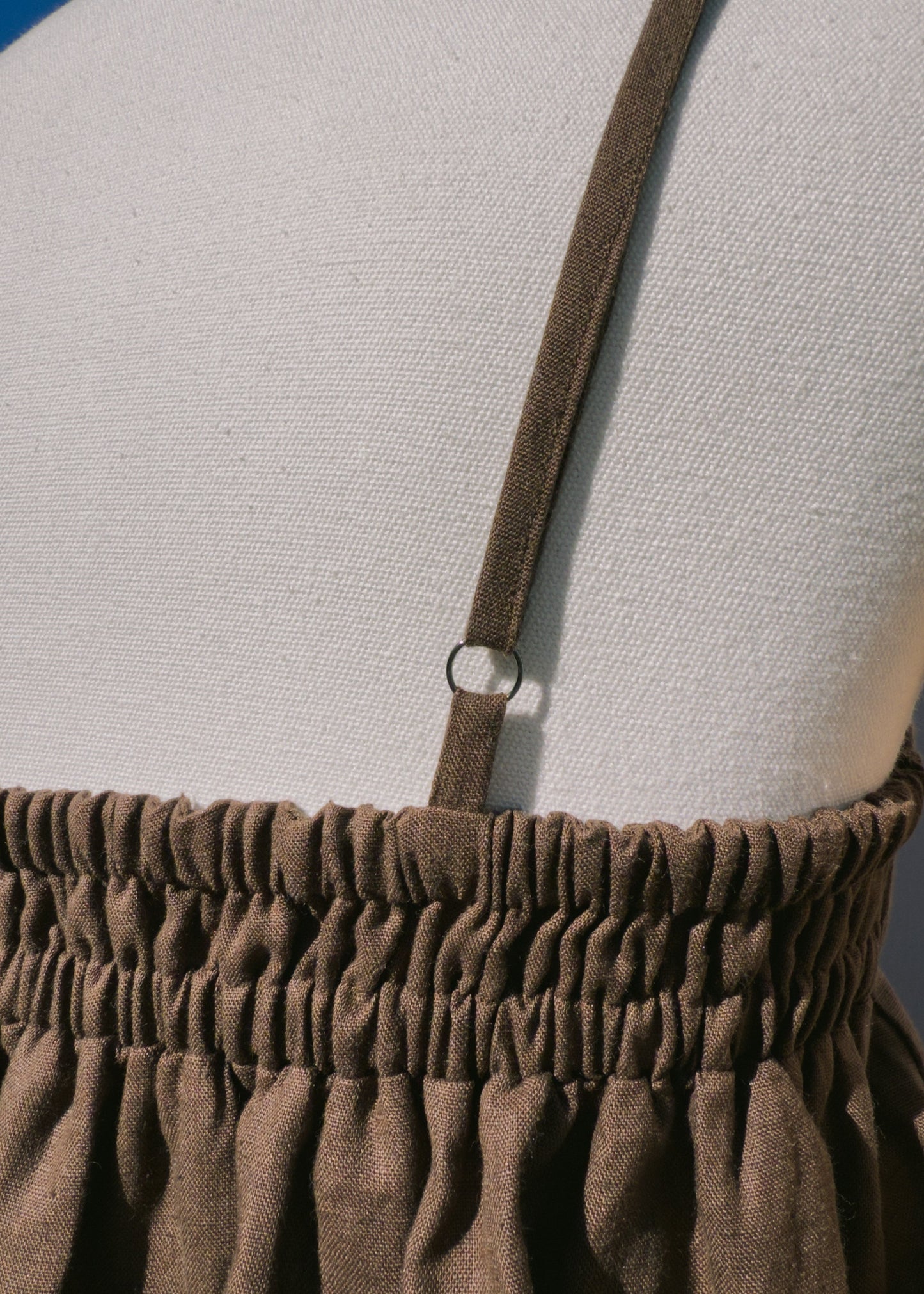 Close up of brown linen top with elastic section on a mannequin in front of a plain beige background