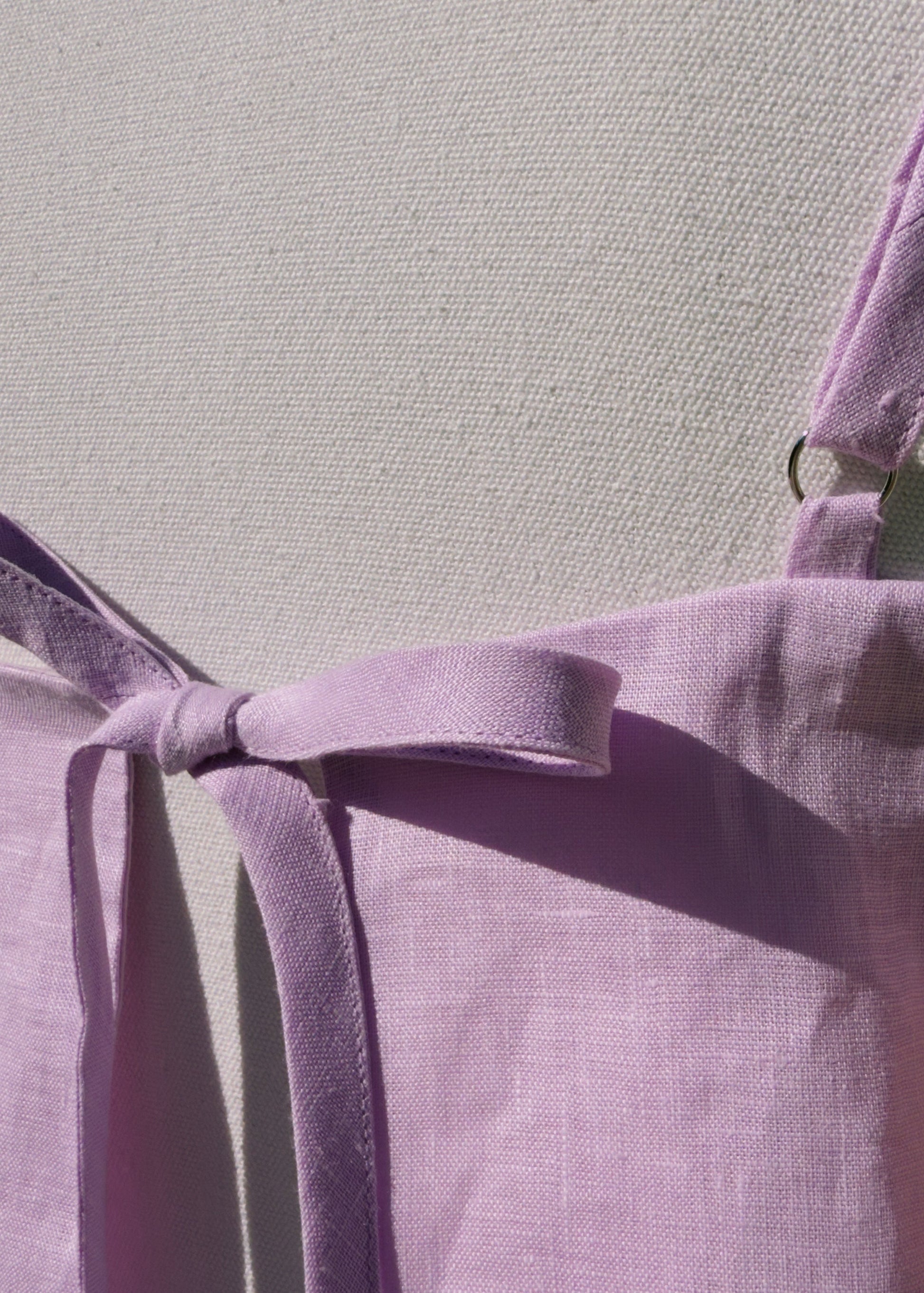 Close up of back tie of lilac linen top on a mannequin in front of a plain beige background