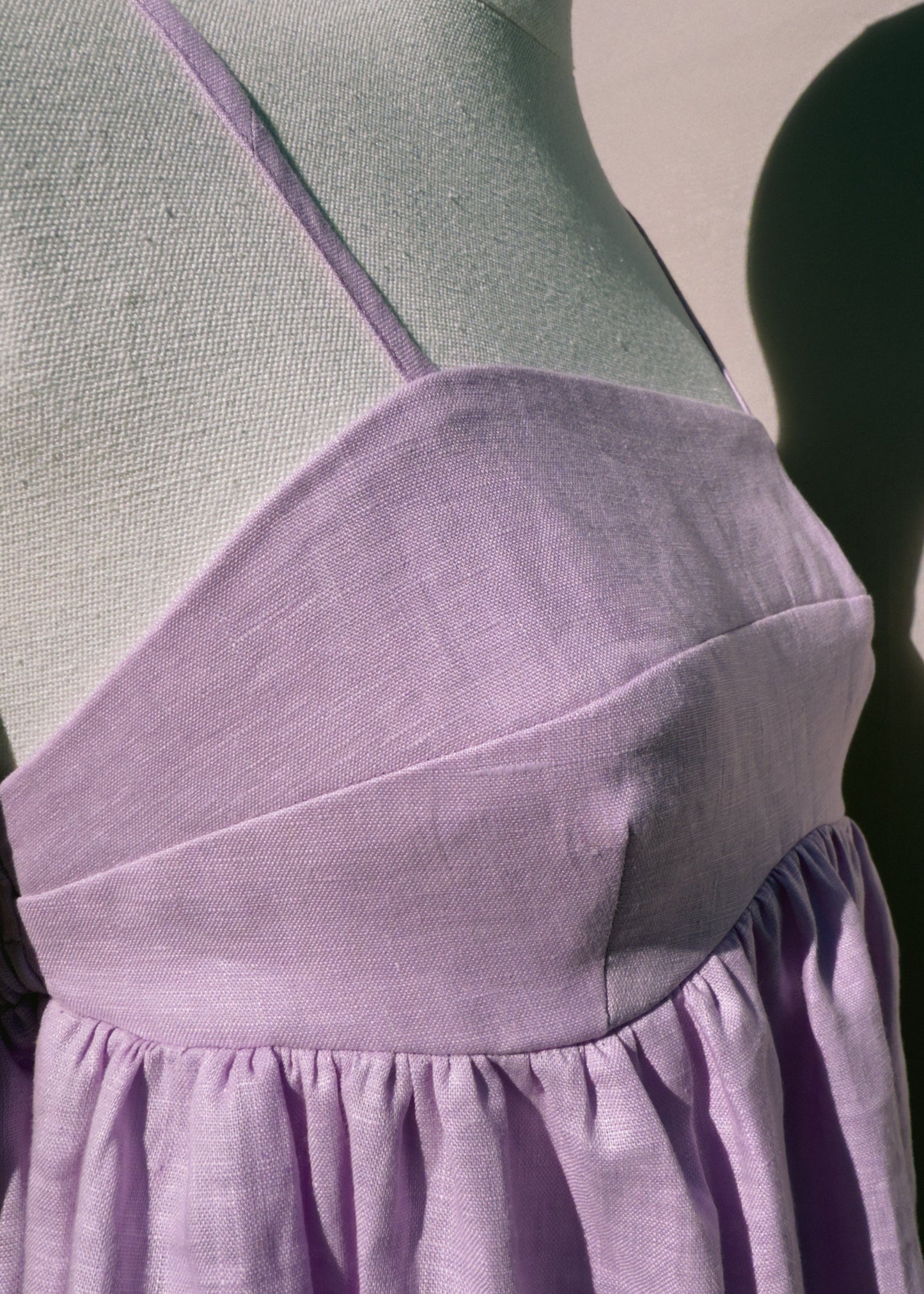 Side view of lilac linen top with gathers on a mannequin in front of a plain beige background