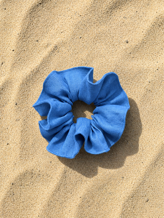 A bright blue fabric scrunchie placed on a textured sandy surface.