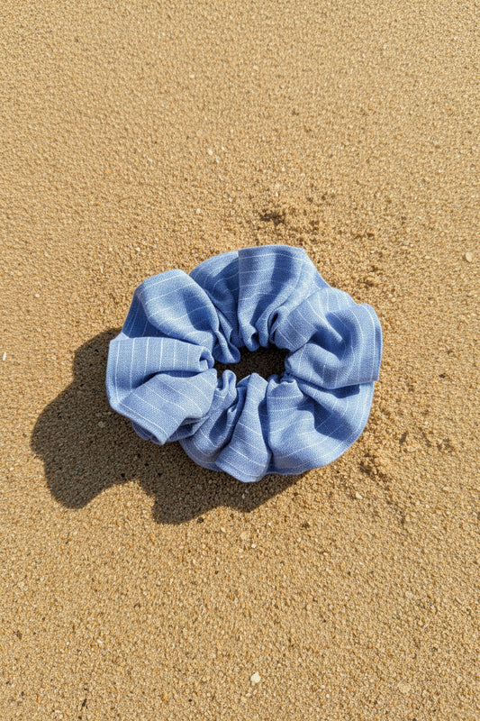 A light blue striped fabric scrunchie resting on the center of a black tablet, held by a hand over a floral-patterned surface.