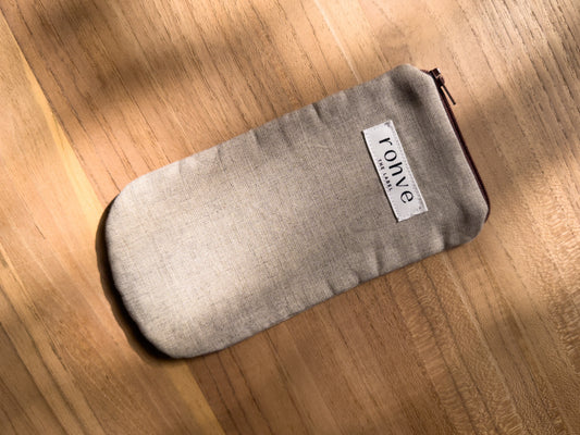 A beige linen fabric zippered pouch with a white brand label reading 'rohve' and a brown zipper, placed diagonally on a warm wooden surface.