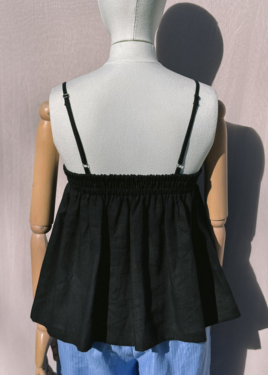 Back of black linen top with gathers on a mannequin in front of a plain beige background