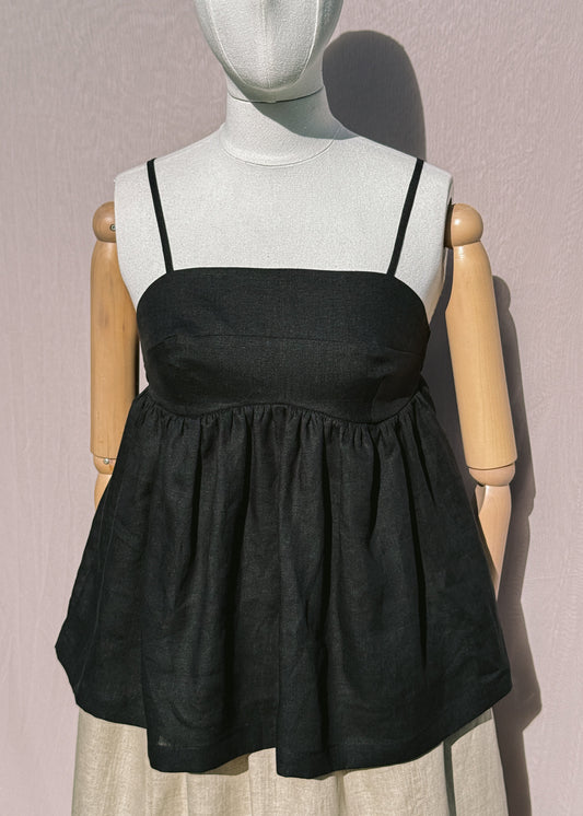 Black linen top with gathers on a mannequin in front of a plain beige background