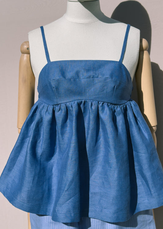 Blue linen top with gathers on a mannequin against a plain background