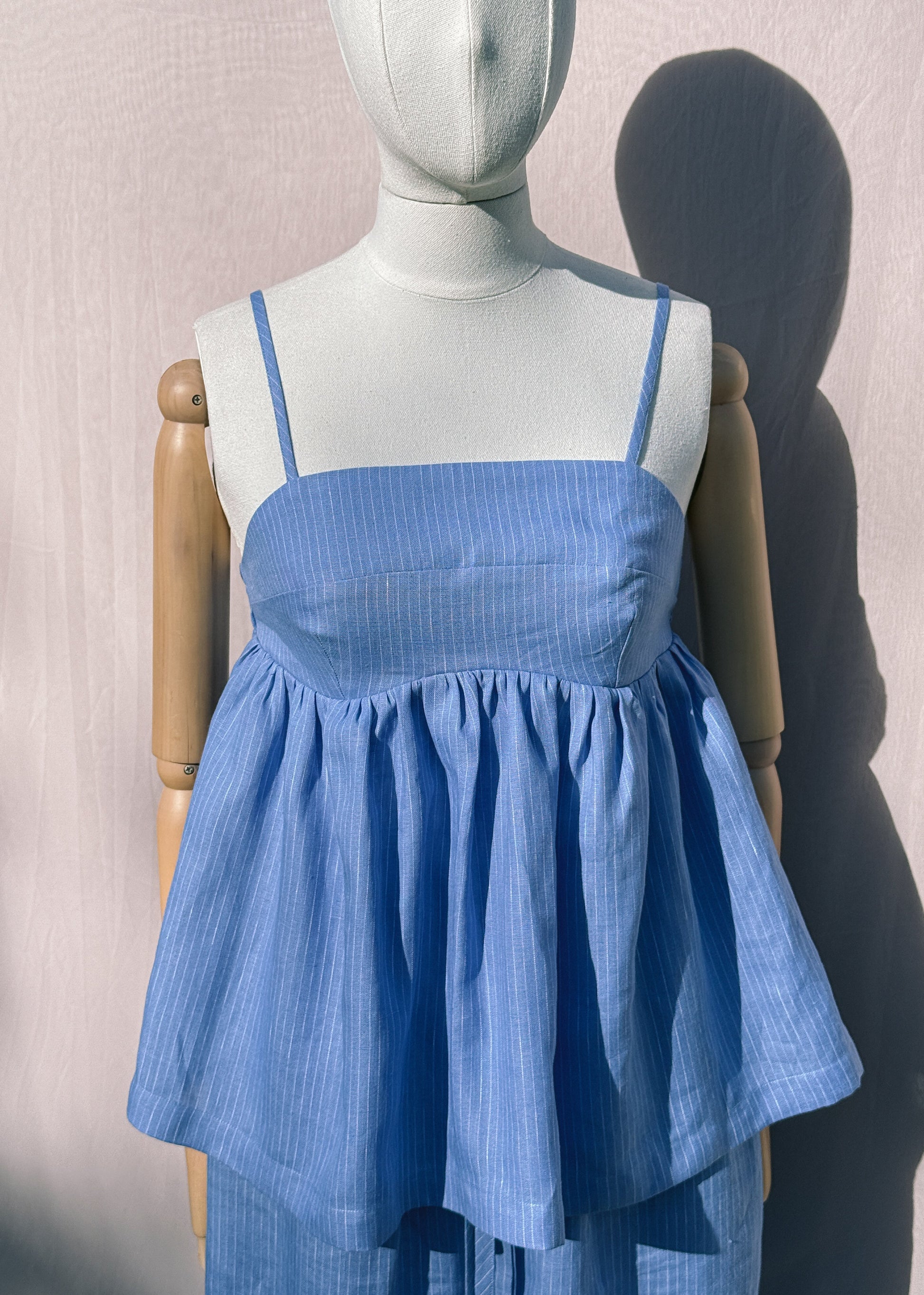 Blue striped linen top with gathers on a mannequin in front of a plain beige background