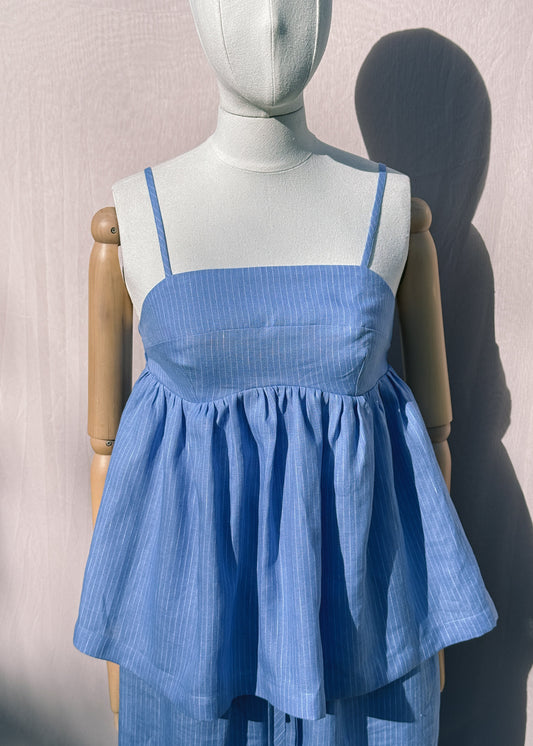 Blue striped linen top with gathers on a mannequin in front of a plain beige background