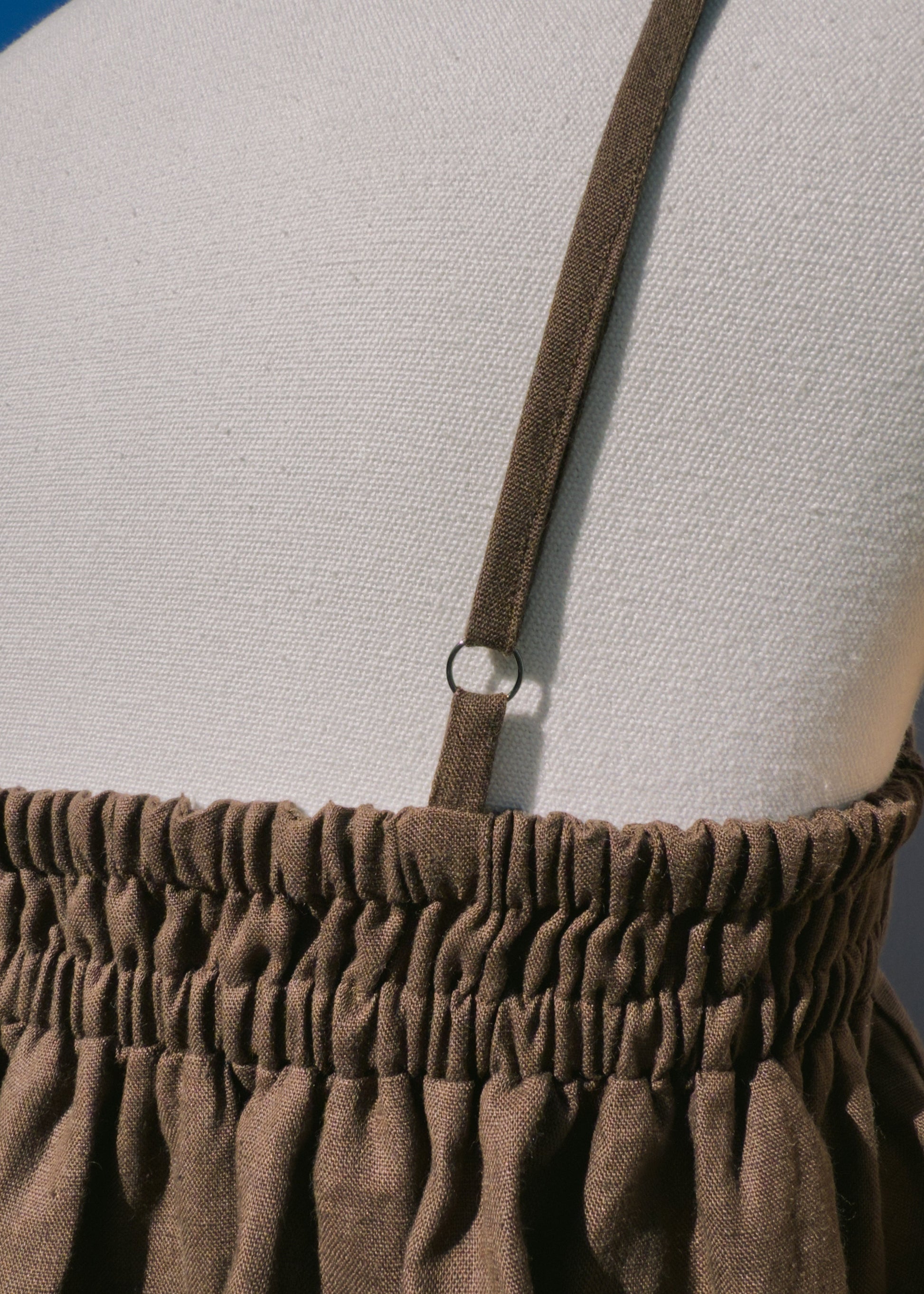 Close up of brown linen top with elastic section on a mannequin in front of a plain beige background