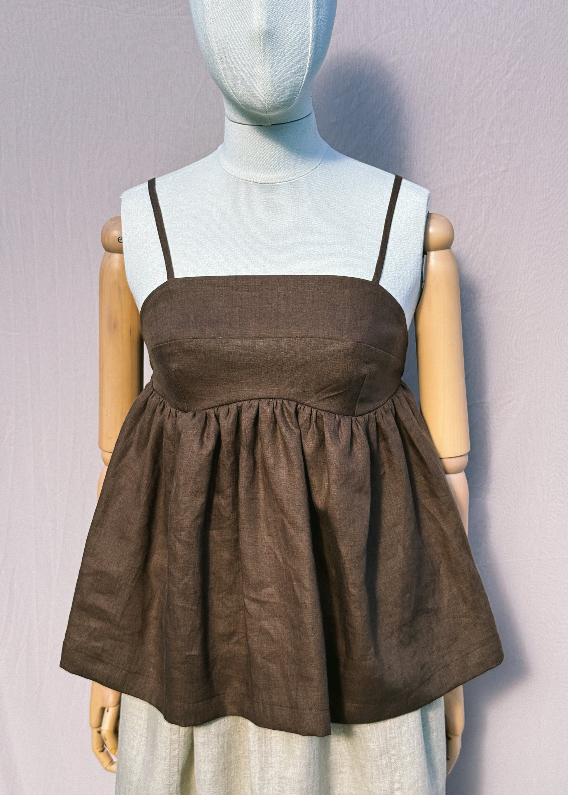 Brown linen top with gathers on a mannequin in front of a plain beige background