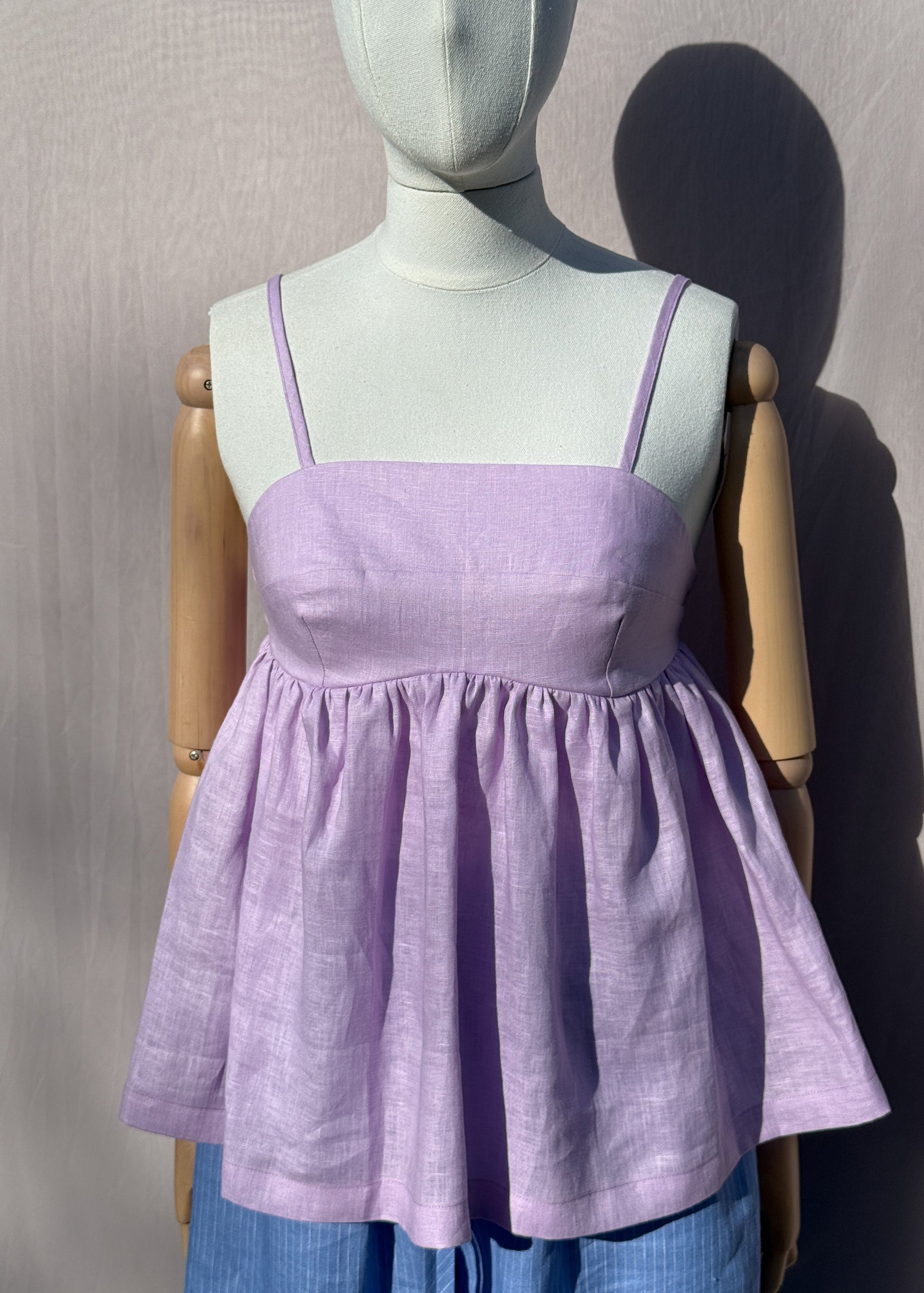 Lilac linen top with gathers on a mannequin in front of a plain beige background
