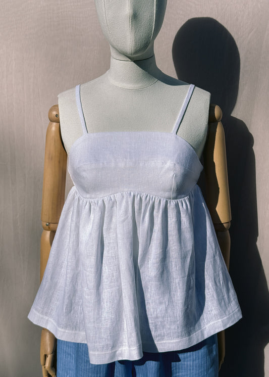 White linen top with gathers on a mannequin in front of a plain beige background