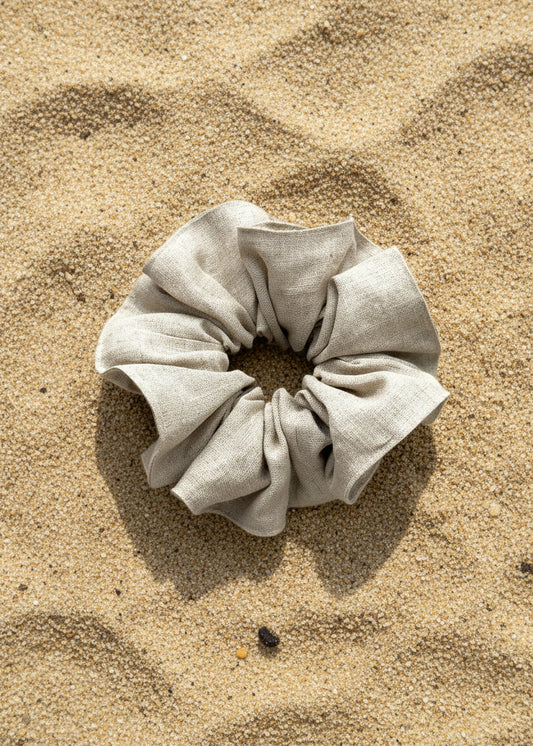 A light beige linen scrunchie resting on a sandy beach background.