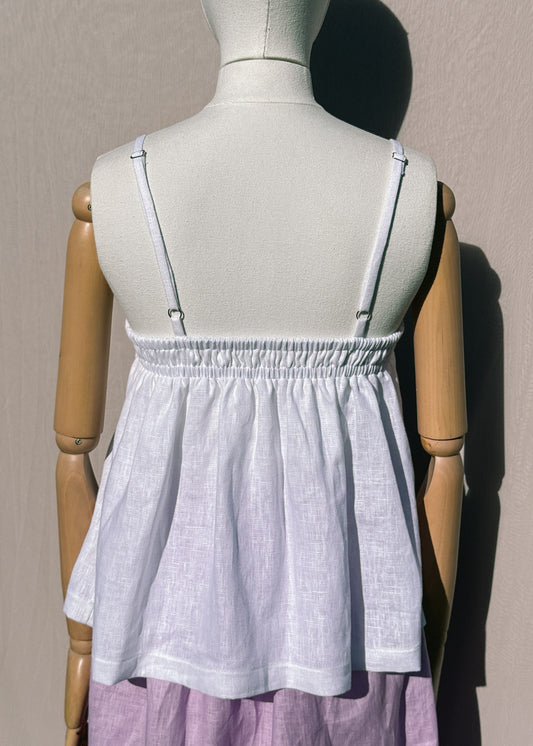 White linen top with elastic channels on a mannequin in front of a plain beige background